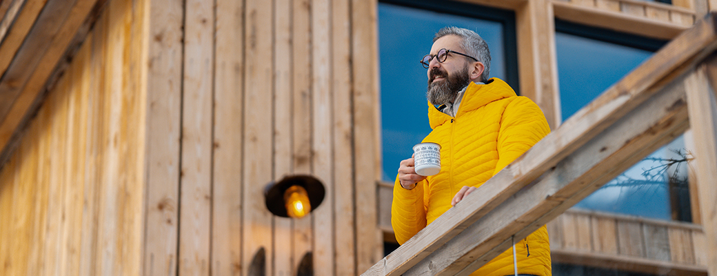 Image of middle-aged man holding a cup of coffee while looking out from his outdoor deck 